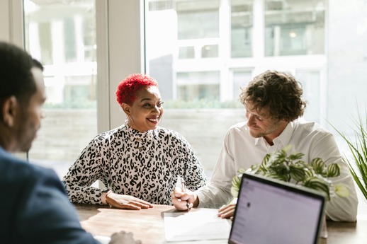 Financial planners seated around a wooden office table with a laptop and documents, collaborating on CFP® certification steps in a bright, modern workspace with natural light.